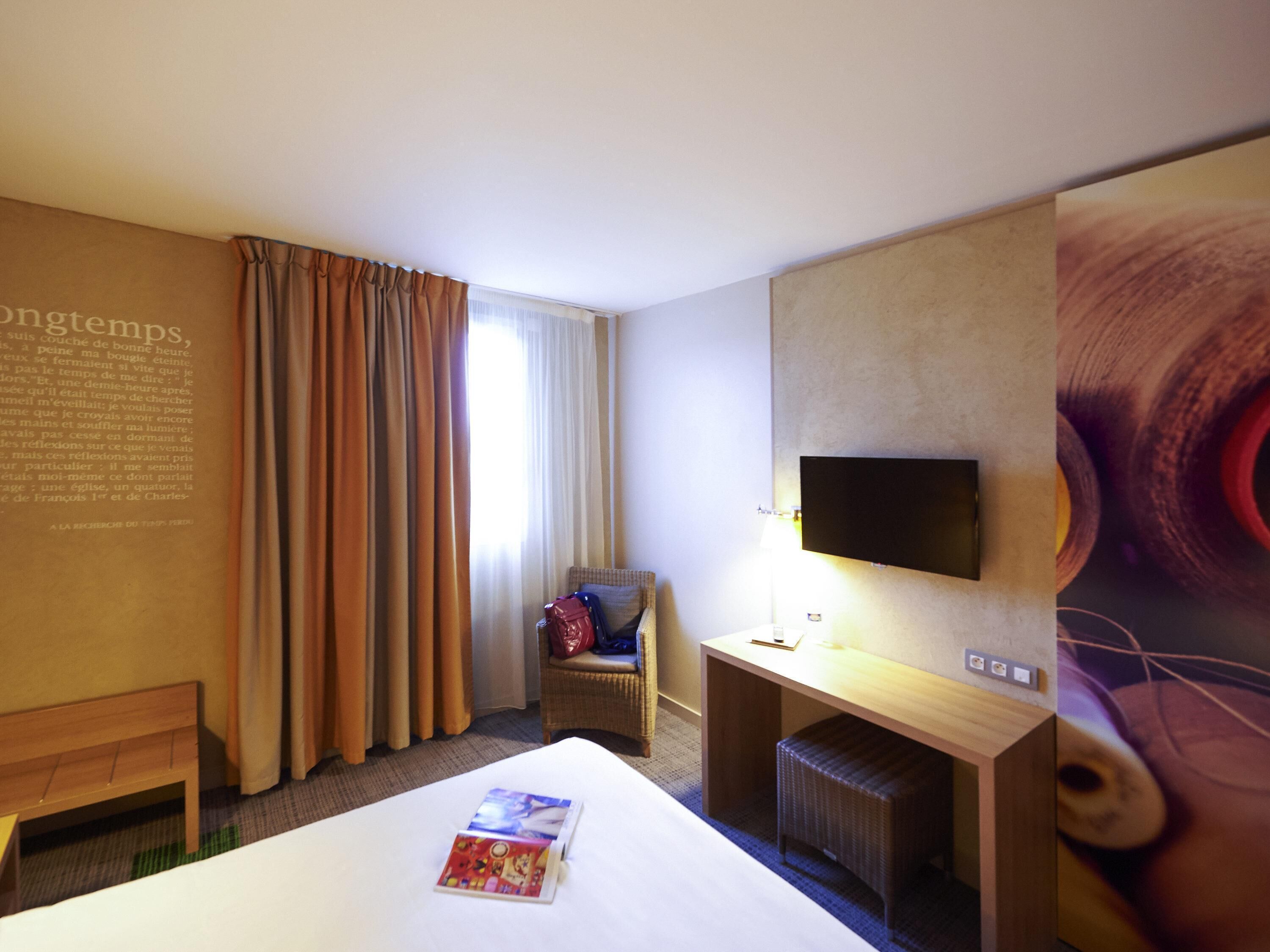Une chambre d’hôtel avec un lit, une chaise, un bureau, une télévision et un mur avec du texte.