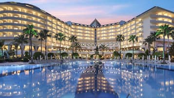A hotel with a large pool, multiple balconies, and palm trees.