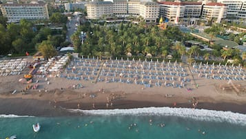 A beach resort with multiple hotel buildings, a large beach area with numerous umbrellas and lounge chairs, and a view of the ocean.