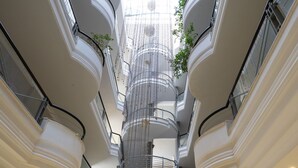 Un atrio de varios niveles con una escalera central, barandillas de vidrio y una zona de recepción.