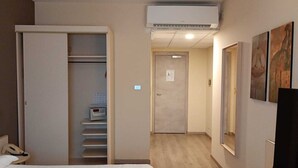 A hotel room with a bed, a desk, a wardrobe, and an air conditioning unit. - Hotel Des Alpes (Rosta)