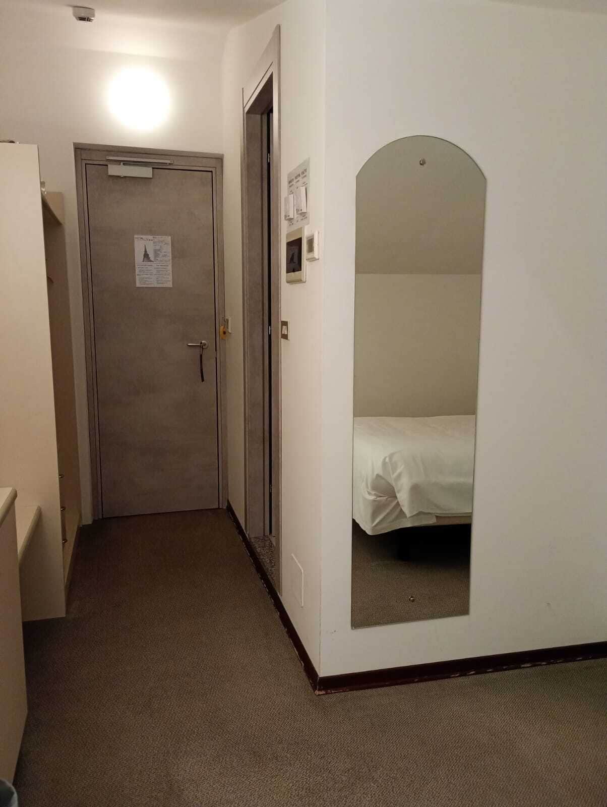 Un pasillo estrecho con una puerta al final que da a una habitación con una cama.