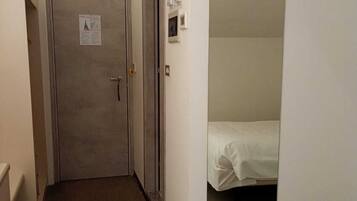 Un pasillo estrecho con una puerta al final que da a una habitación con una cama.