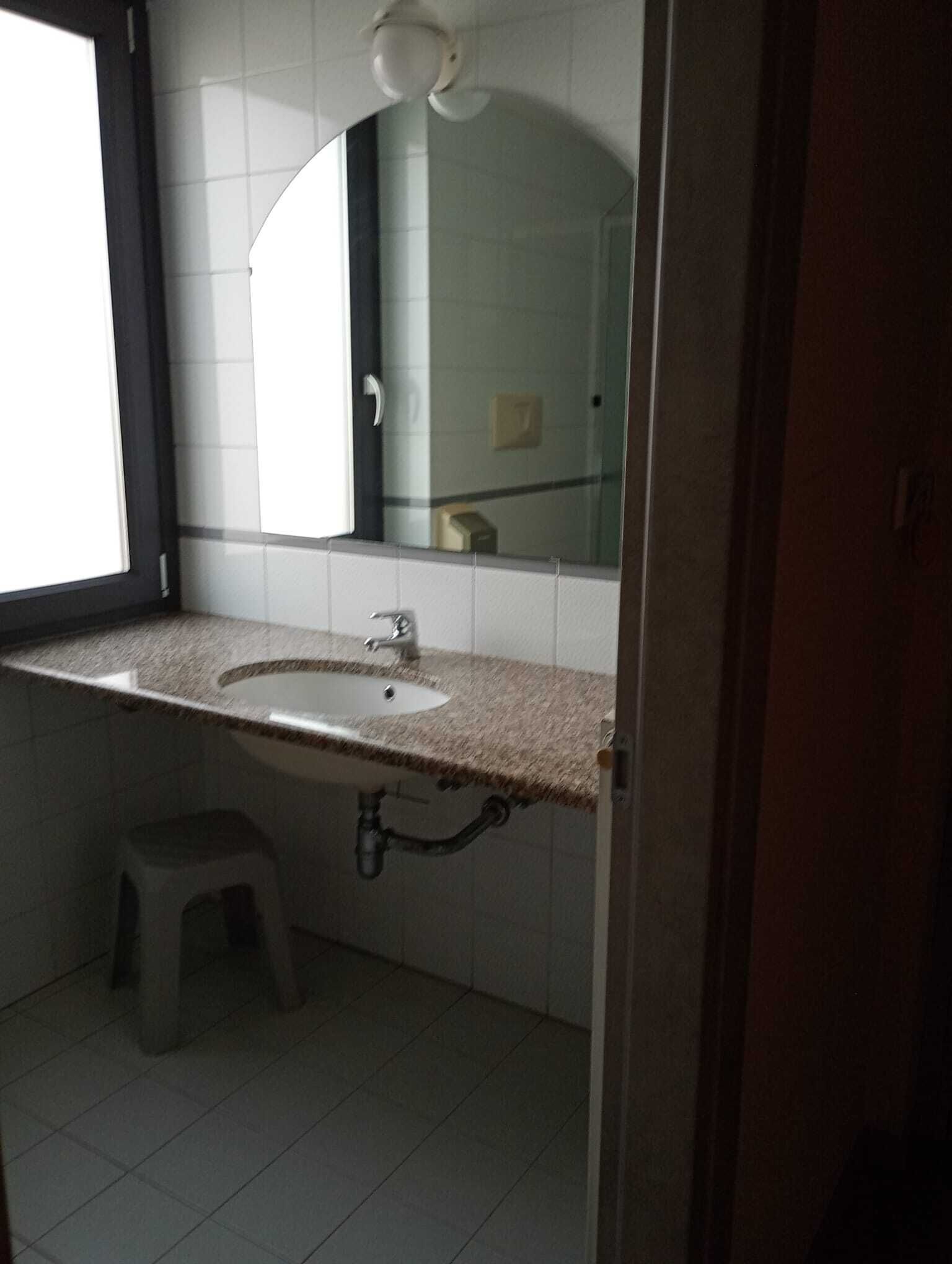 A bathroom with a white sink, a mirror, and a small stool.