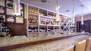 A bar area with granite countertops, bar stools, and shelves stocked with various bottles. - Hotel Des Alpes (Rosta)