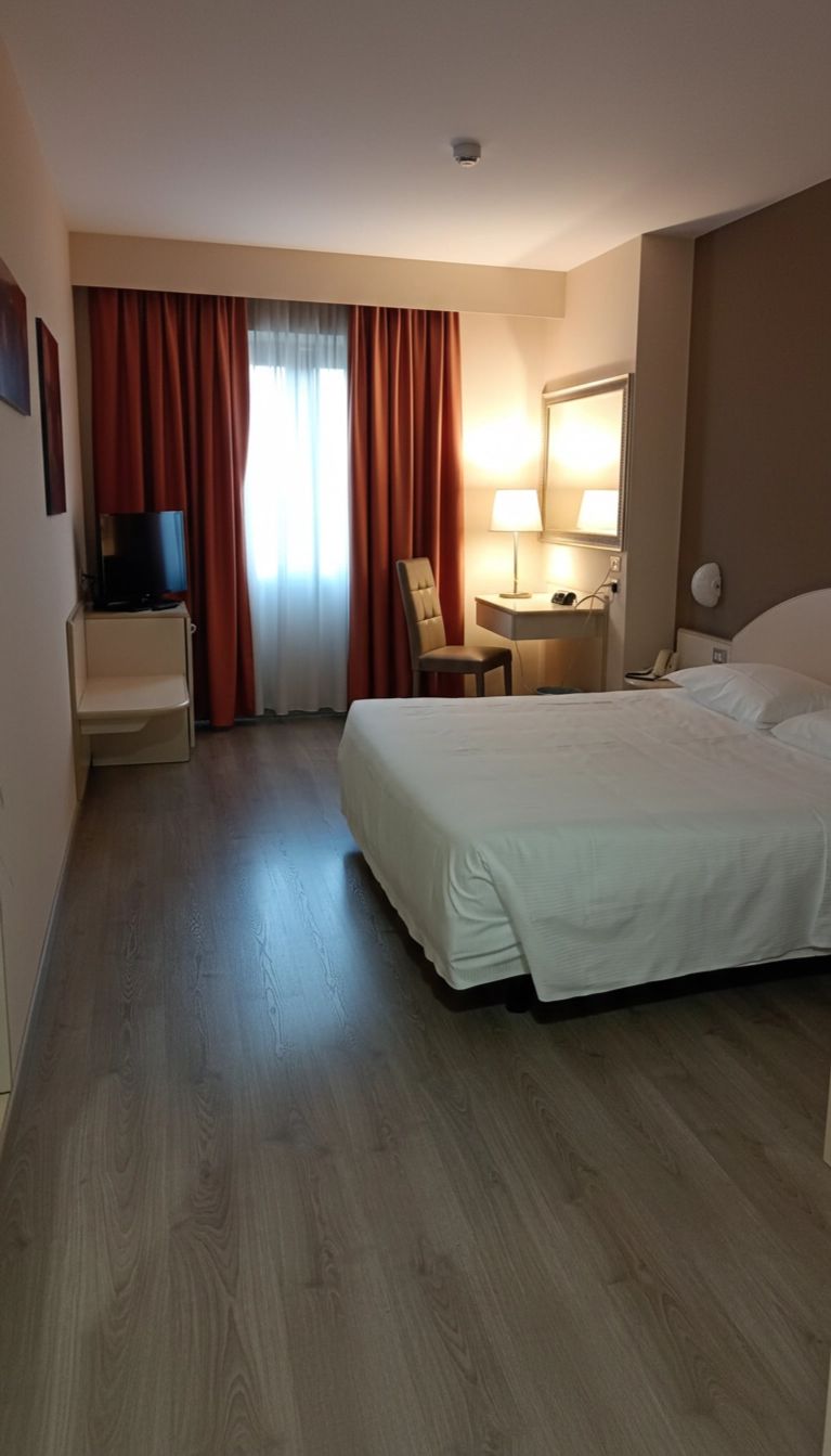 Ein Hotelzimmer mit einem Bett, einem Schreibtisch, einem Sessel, einem Fernseher und einem Fenster mit Vorhängen.