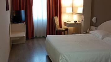 A hotel room with a bed, a desk, a chair, a TV, and a window with curtains.