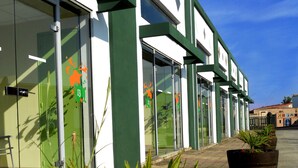 A building with large glass windows and green-framed doors, a paved entrance, and potted plants with flowers. -  In Jungle hôtel (Beauvallon)