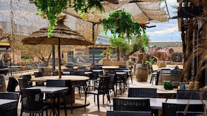 An outdoor dining area with tables and chairs, thatched umbrellas, and decorative plants. -  In Jungle hôtel (Beauvallon)