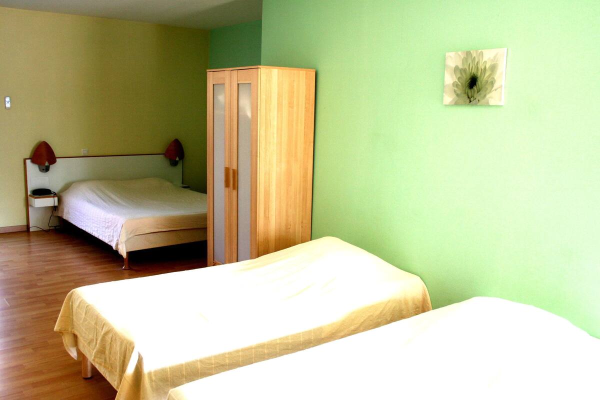 A room with two single beds, a wooden wardrobe, a nightstand, and a wall-mounted lamp.