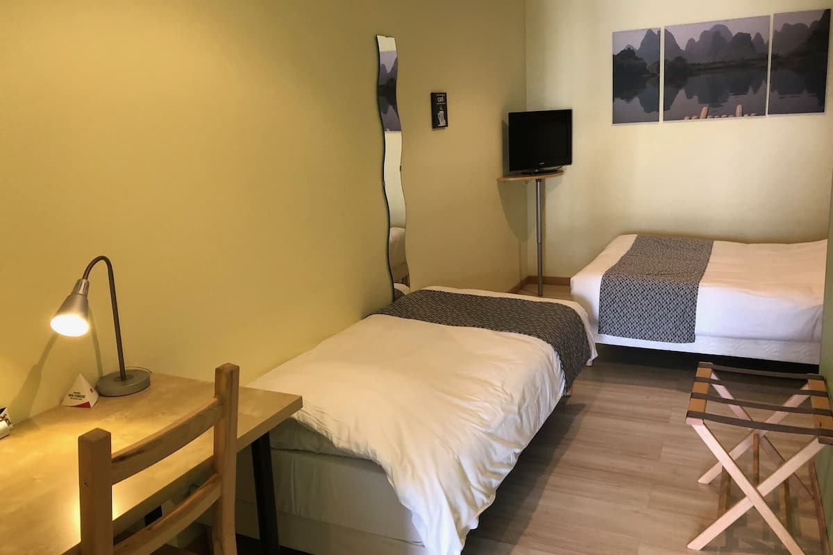 A small, cozy room with two beds, a desk, a chair, a TV, and a painting on the wall.