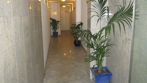 Un couloir avec un sol carrelé, des plantes en pot et un panneau indiquant la réception.