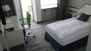 Une chambre d’hôtel avec un lit, un bureau, une chaise et une fenêtre avec des rideaux.