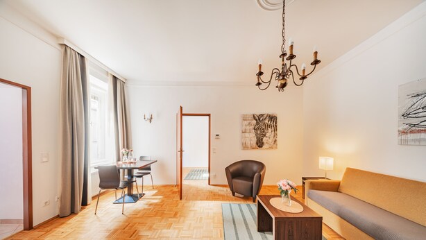 Ett modernt vardagsrum med en soffa, ett soffbord, en matplats med bord och stolar, en kristallkrona och konstverk på väggarna.
