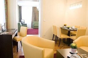 Quarto de hotel com área de refeições, um sofá e uma pequena mesa com um vaso de flores.