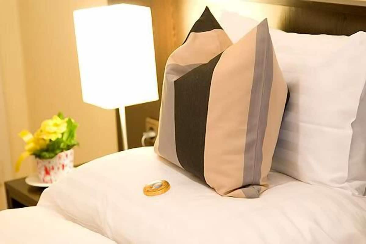 A neatly made bed with white bedding and two decorative pillows, a bedside table with a lamp, and a small vase with flowers.