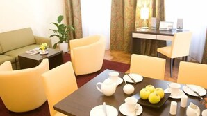 Ett hotellrum med en soffa, ett matbord dukat med te och äpplen, ett skrivbord med en dator och högtalare samt en krukväxt.