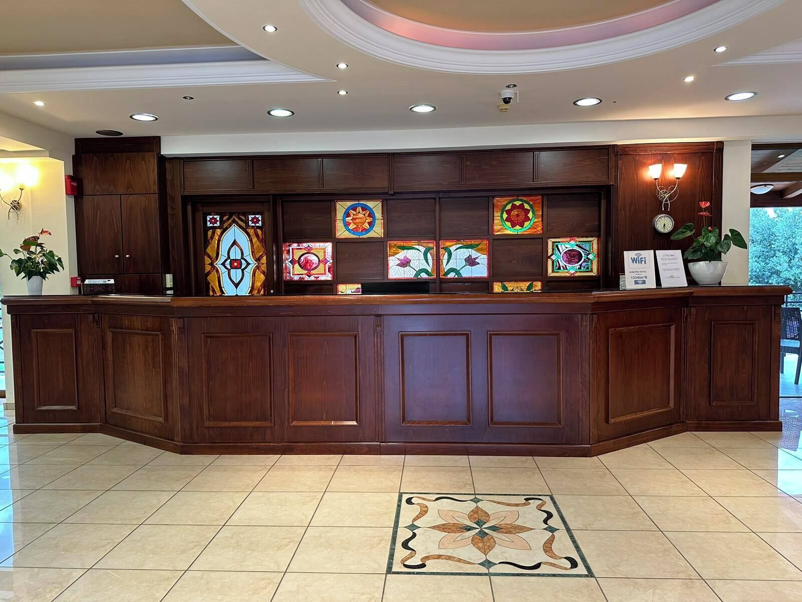 Un mostrador de recepción con detalles de madera, piso de baldosas y una ventana de vidrio emplomado decorativa sobre él.