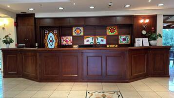 Un mostrador de recepción con detalles de madera, piso de baldosas y una ventana de vidrio emplomado decorativa sobre él.