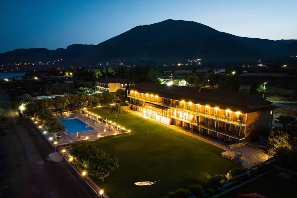 A large hotel with a swimming pool, well-lit outdoor areas, and a mountain in the background.