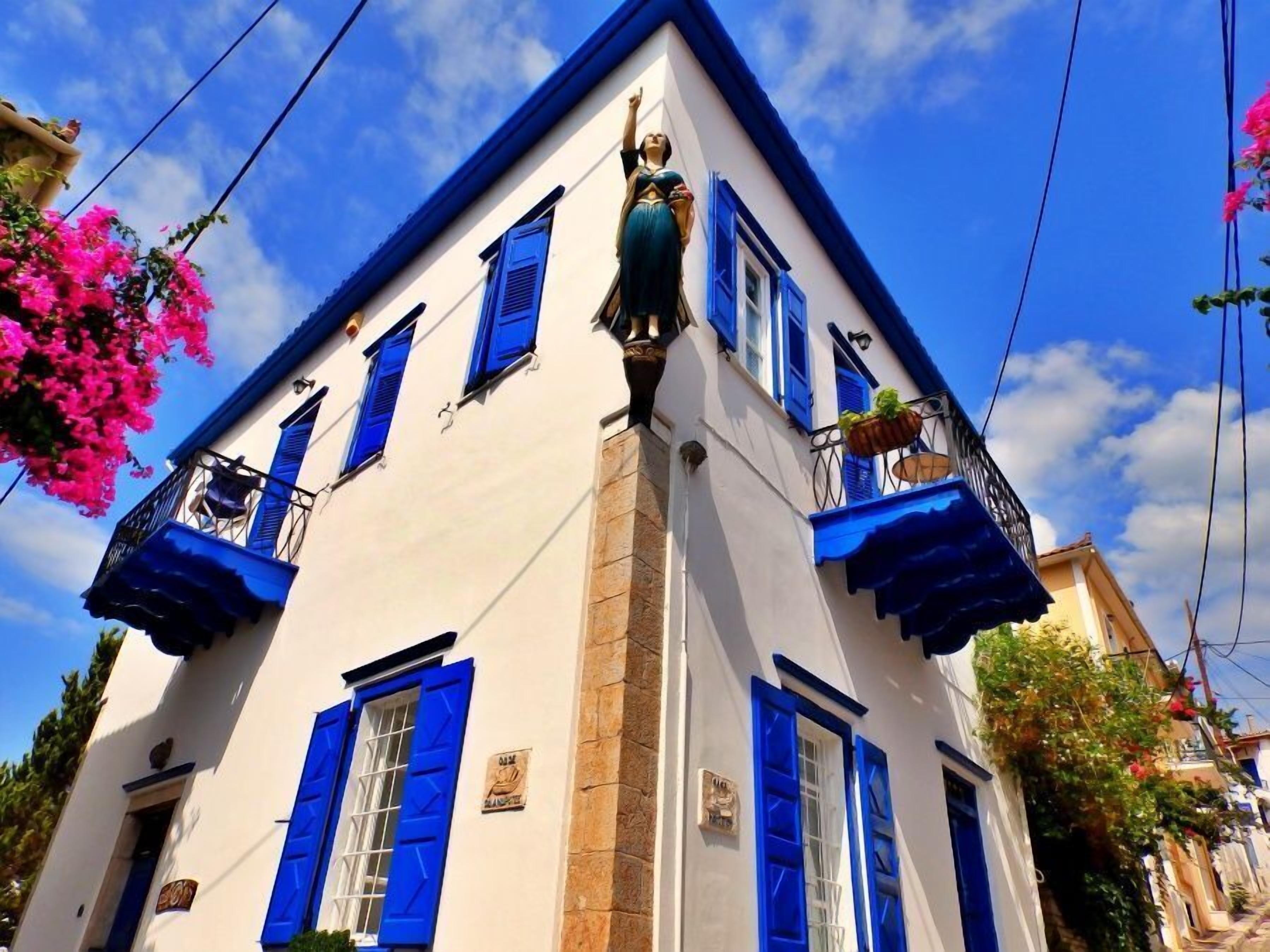 A building with blue shutters and balconies, white walls, and a clear blue sky.