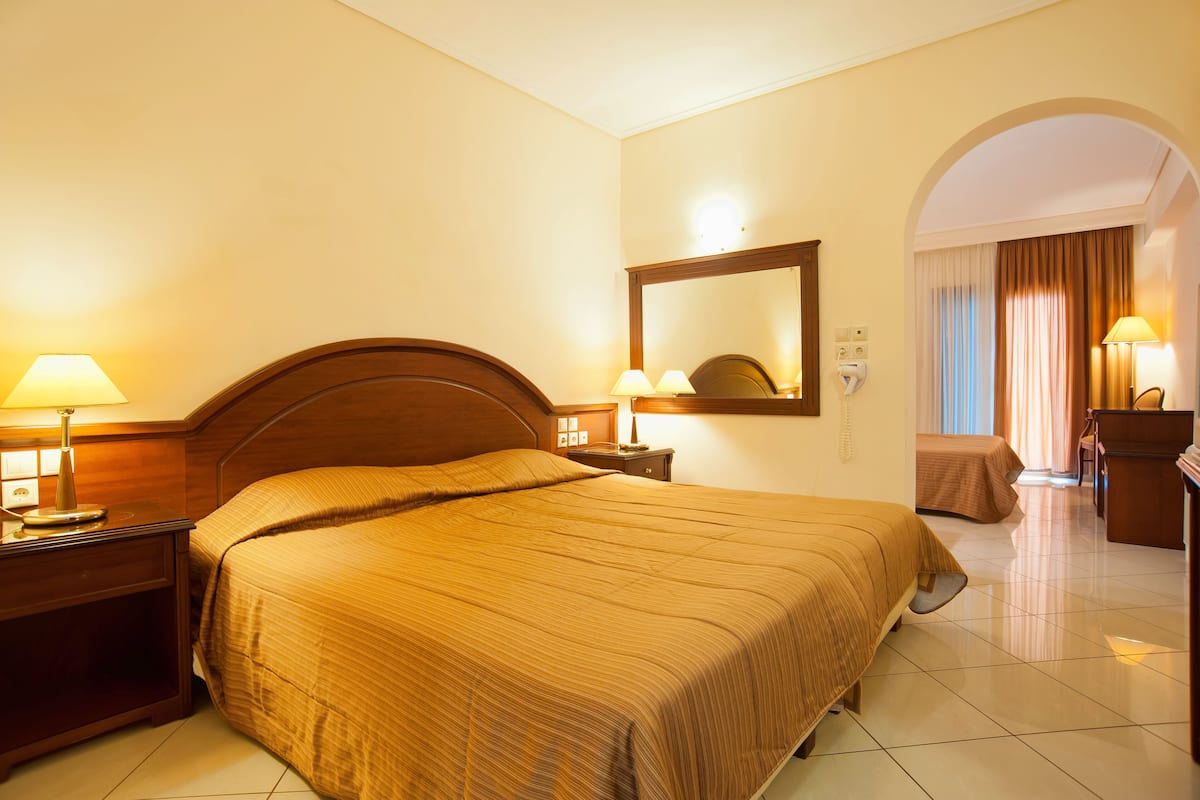 A hotel room with a large bed, two bedside tables with lamps, a mirror, a desk with a chair, and an arched doorway.