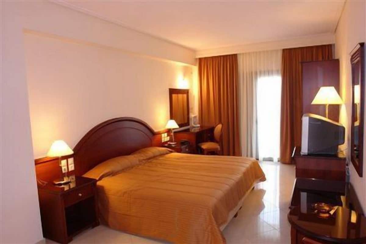 A hotel room with a large bed, two bedside tables with lamps, a desk with a chair, and a television.