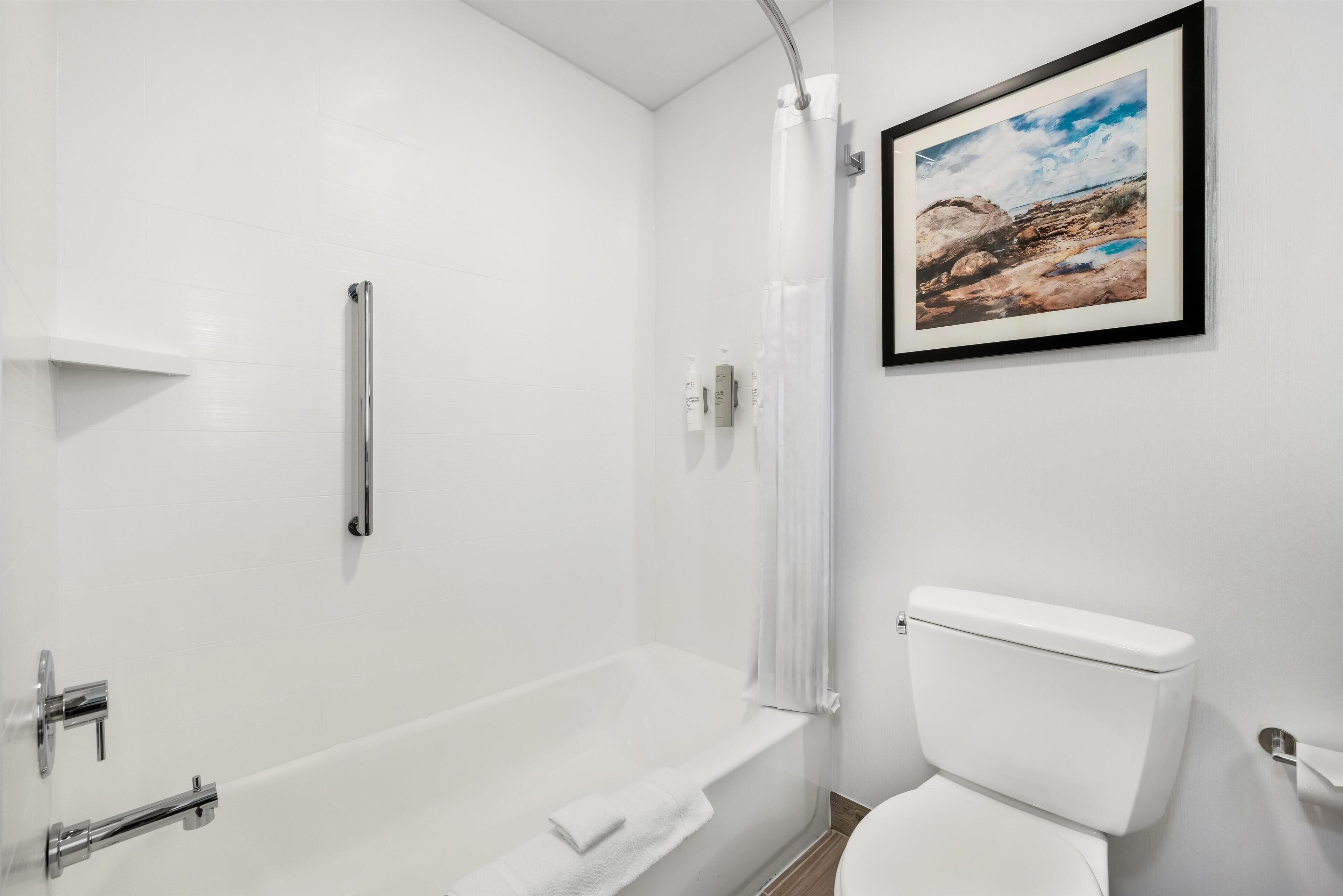 A bathroom with a white bathtub, a toilet, and a framed landscape painting on the wall.