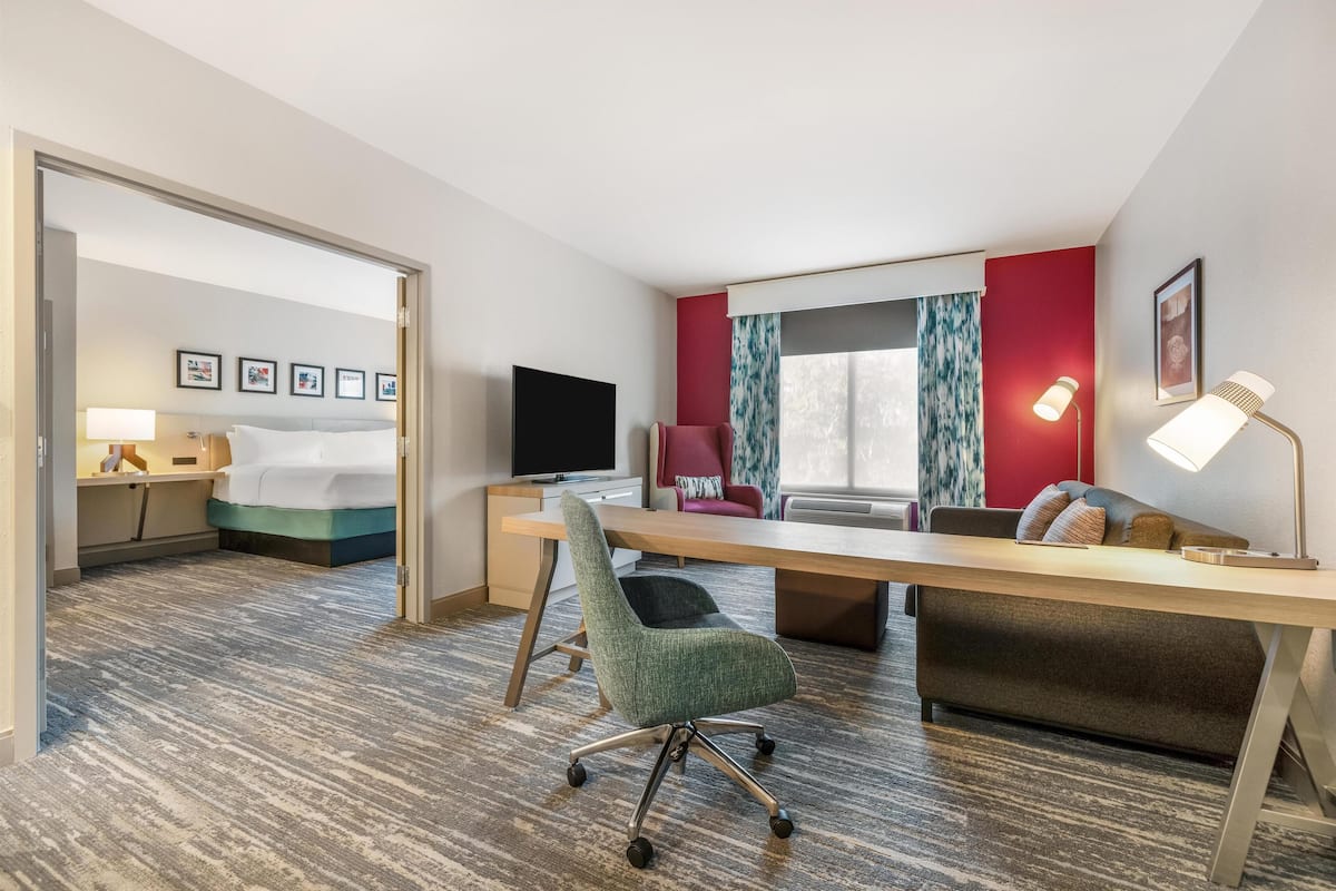 A hotel room with a bed, desk, chair, and a TV.