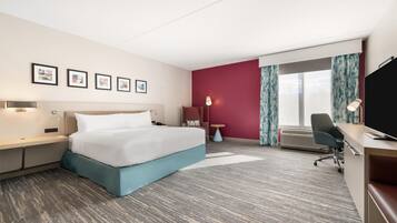 Habitación de hotel con cama, escritorio, silla y ventana grande.