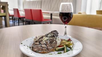 Prato com carne grelhada e legumes, um copo de vinho tinto e uma mesa de jantar em um restaurante.