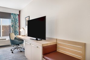 Habitación de hotel con escritorio, silla, televisor y ventana con cortinas.