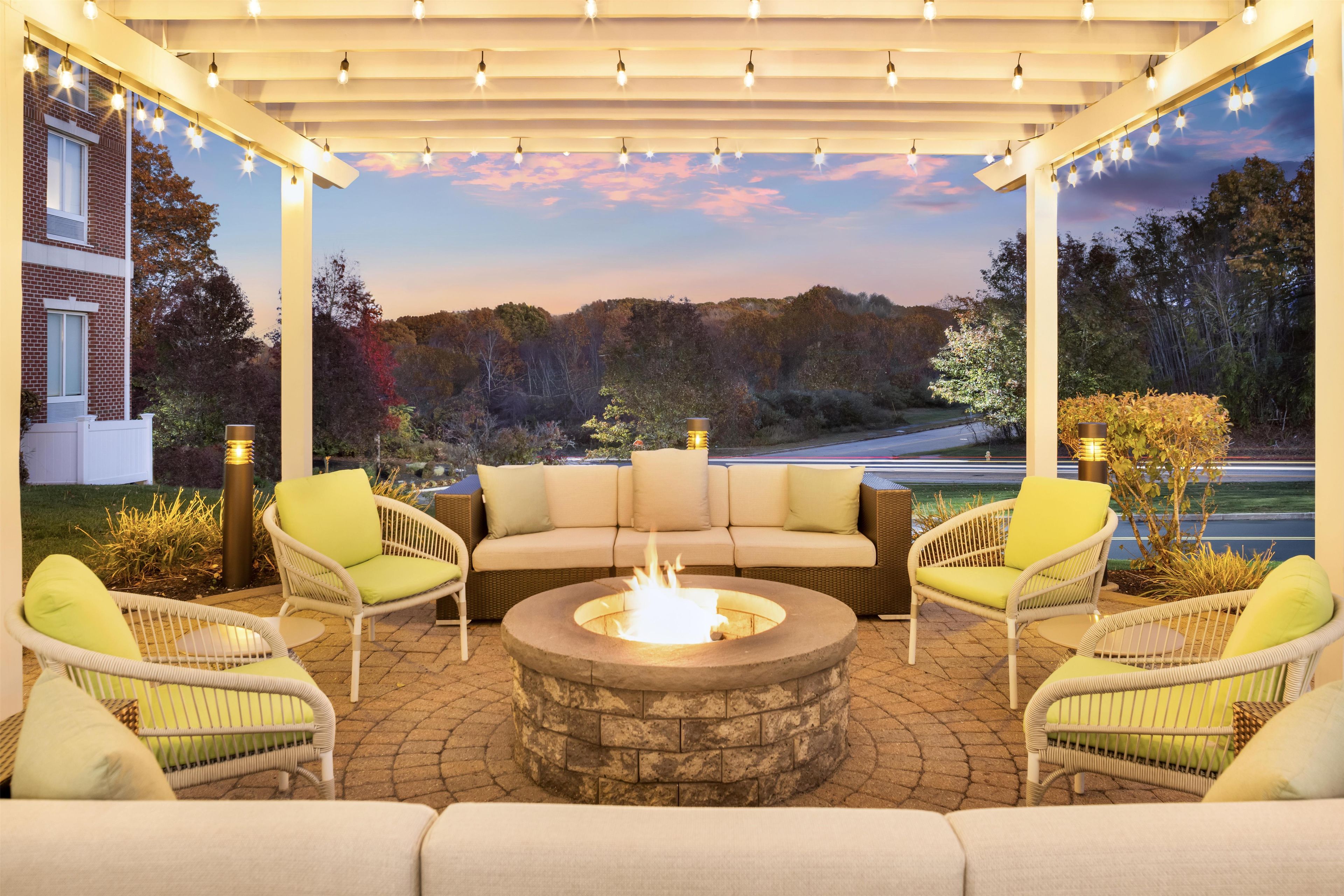 An outdoor patio with a fire pit, seating, and string lights.