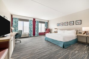 Habitación de hotel con cama, escritorio, silla, televisor y obras de arte en la pared.