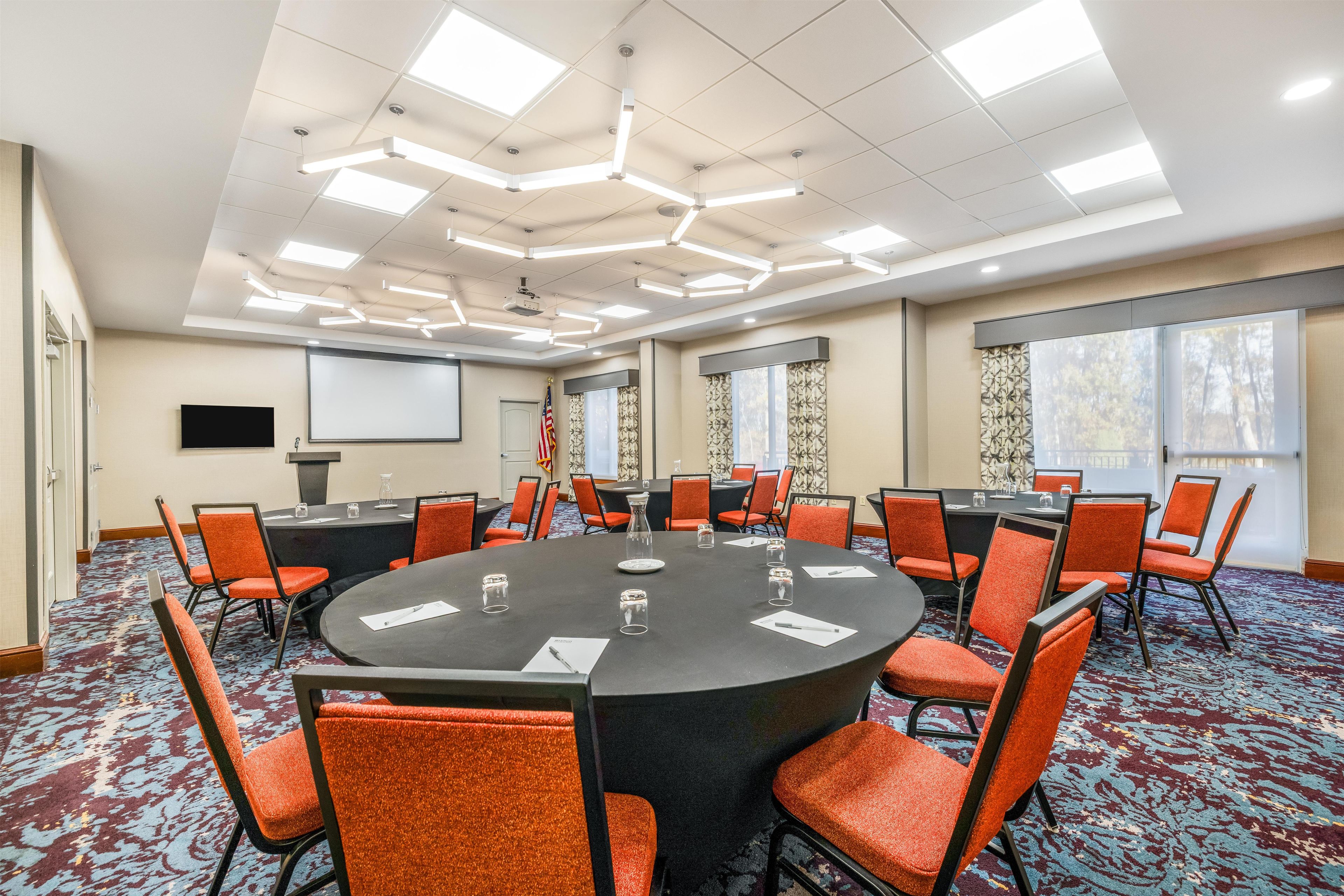 A conference room with a round table, orange chairs, and a projector screen.