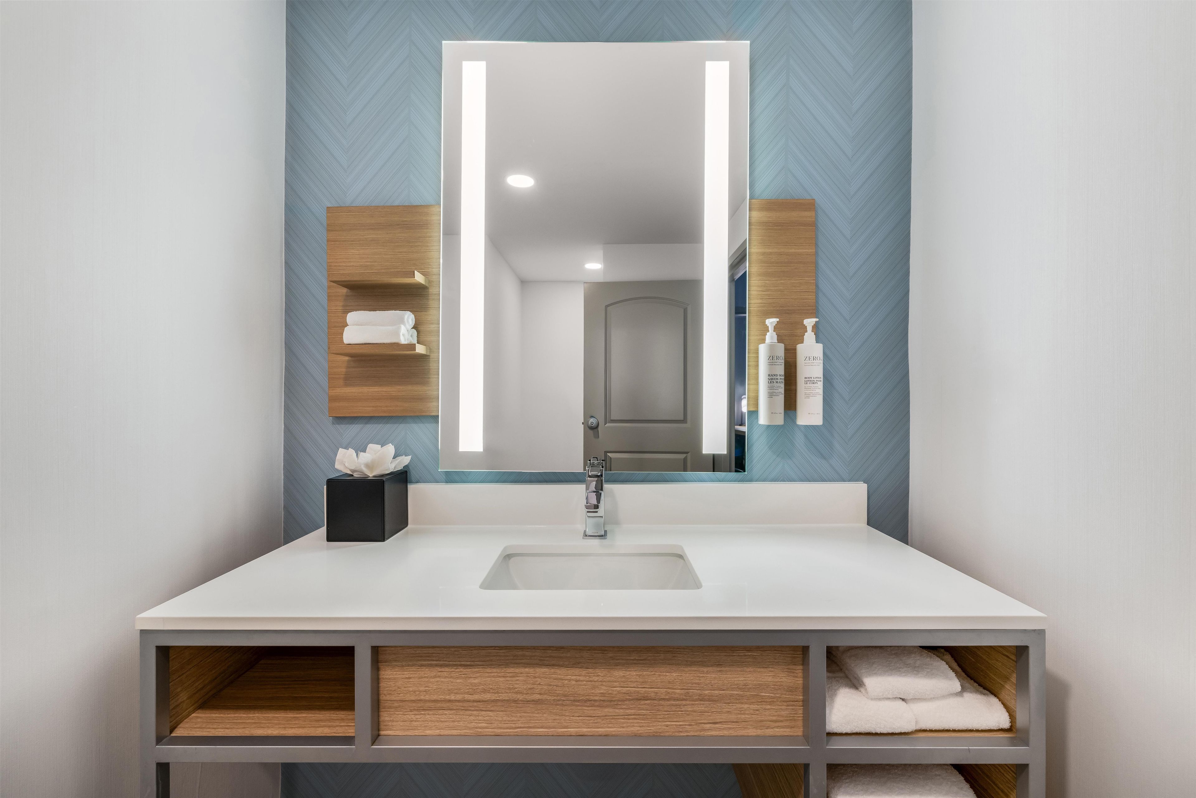 Un baño moderno con un espejo grande, un lavamanos blanco y estantes de madera.