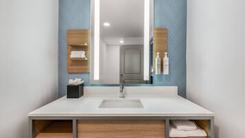 Un baño moderno con un espejo grande, un lavamanos blanco y estantes de madera.
