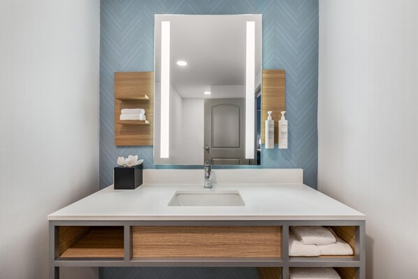 A modern bathroom with a large mirror, white sink, and wooden shelves. - Hilton Garden Inn Mystic/Groton (Groton)