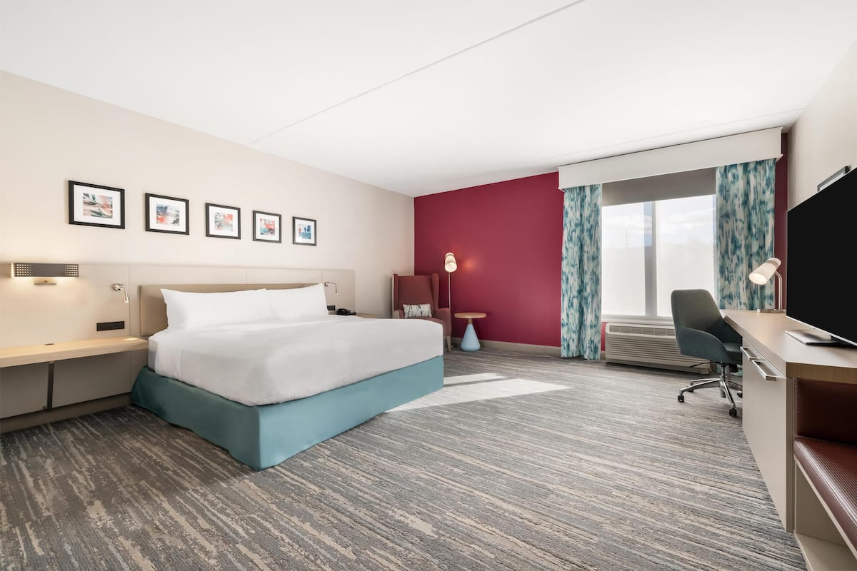 A hotel room with a bed, desk, chair, and large window with curtains.