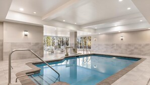 A modern indoor swimming pool with clear blue water, surrounded by light-colored tiles and a metal pool ladder.