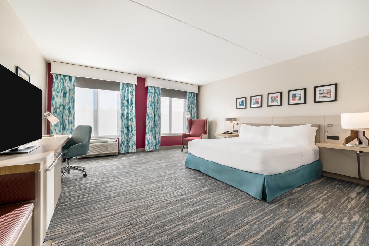 A hotel room with a large bed, a desk with a chair, a TV, and a window with curtains.