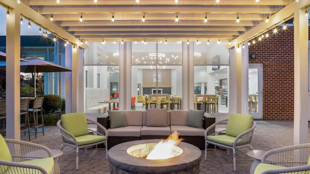 An outdoor patio area with a stone fire pit, wicker furniture, and a modern ceiling with hanging lights.