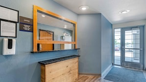 A reception area with a wooden counter, a check-in/out sign, a framed document, and a glass door leading outside.