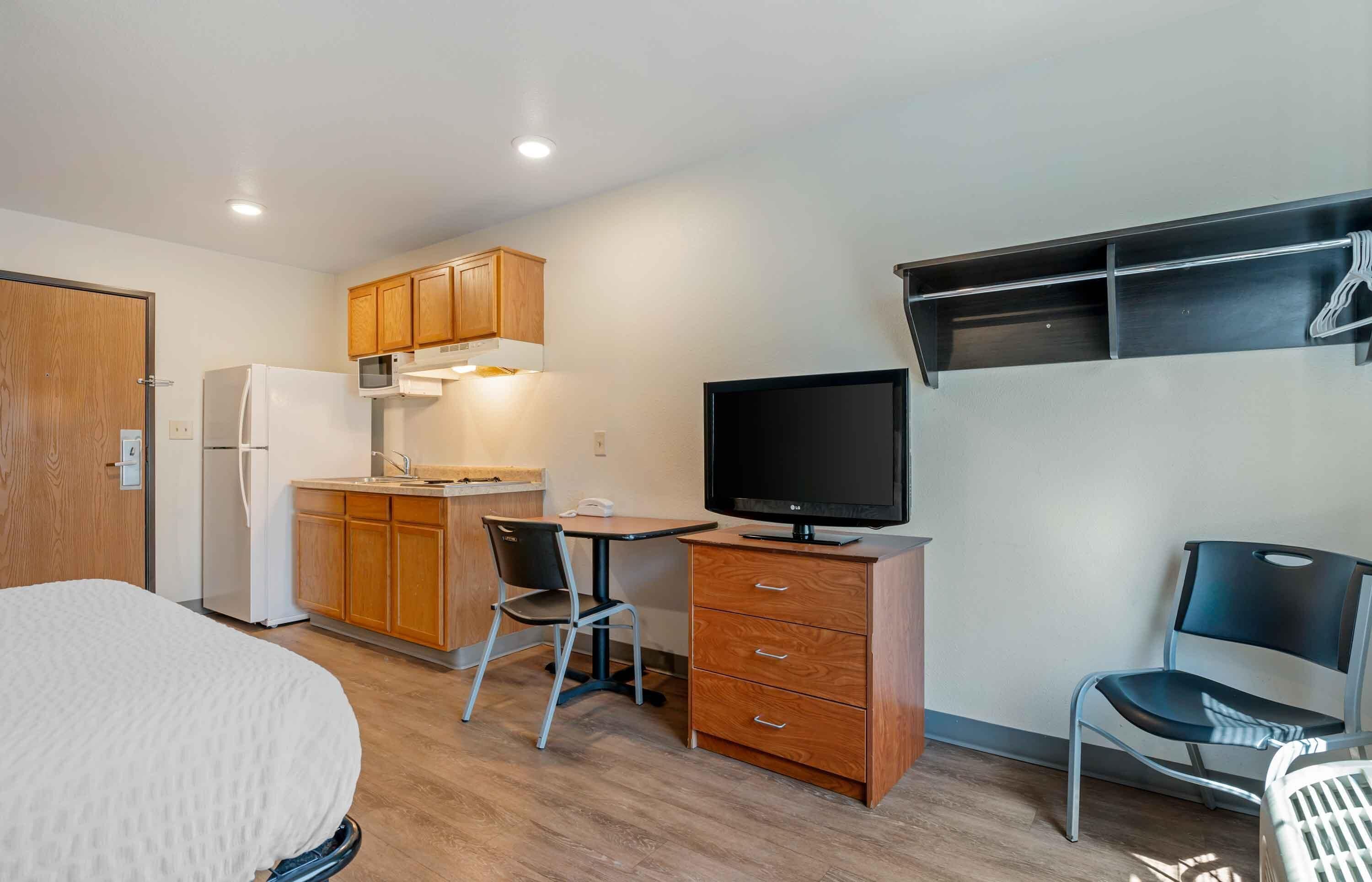 A compact room with a bed, kitchenette, desk, TV, and two chairs.