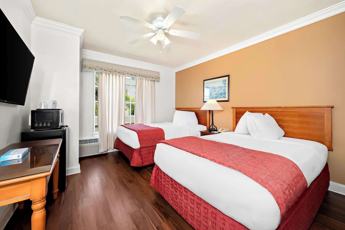 A hotel room with two beds, a desk, a television, and a ceiling fan.