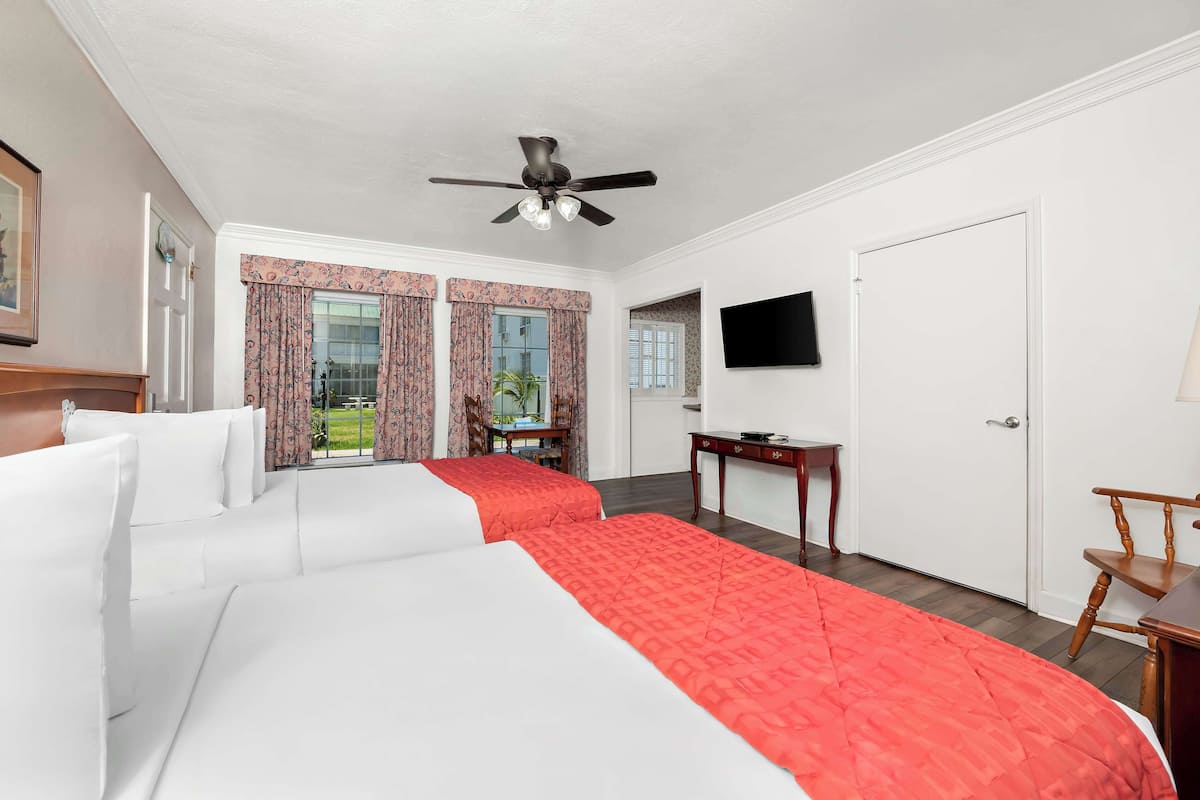 A hotel room with two beds, a ceiling fan, a TV, a desk, and a chair.