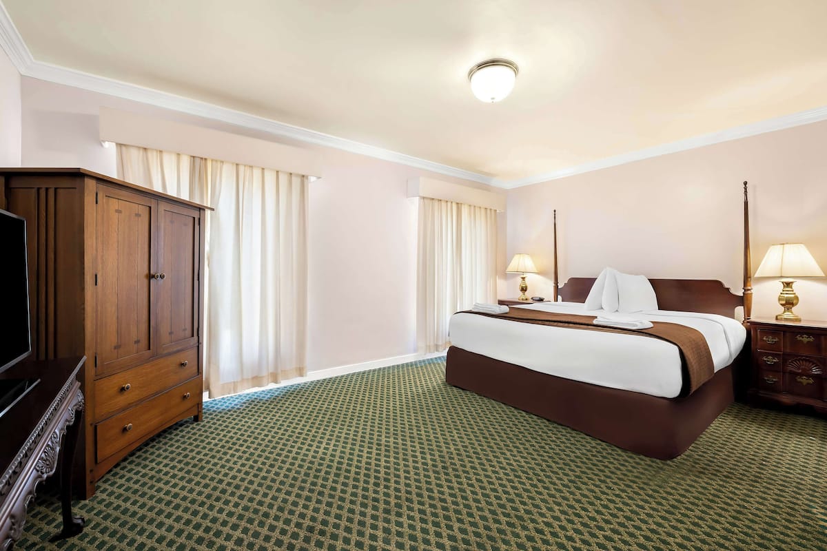 A hotel room with a large bed, a wooden dresser, a television, and two bedside lamps.