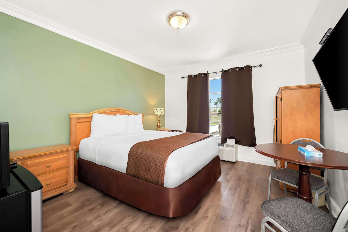 A hotel room with a bed, a desk, a chair, a television, and a window with curtains.