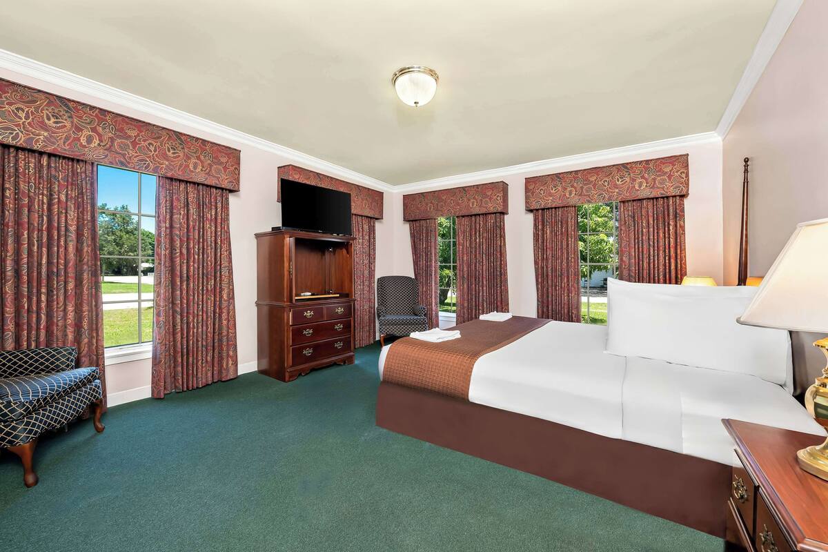 A hotel room with a large bed, a desk with a lamp, a TV, and a chair.