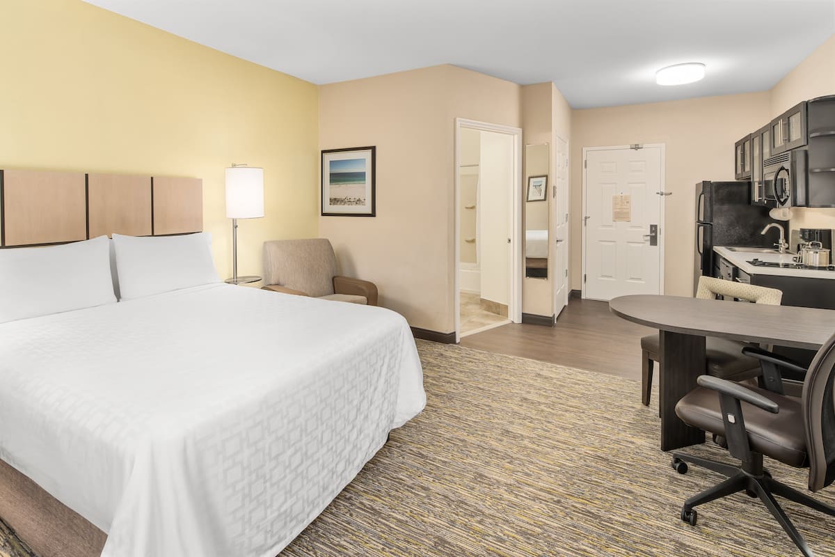 A hotel room with a large bed, a desk, a chair, and a kitchenette.